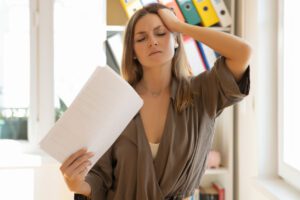 Image of a menopausal woman experiencing a hot flash at home while cooling herself with papers.