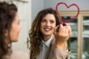 A woman drawing a heart with lipstick on a mirror to illustrate how vaginal tightening surgery can enhance intimacy.