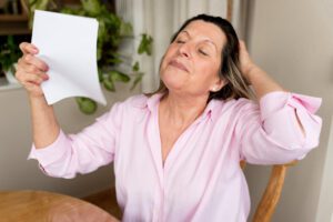 Senior woman fanning herself at home during a hot flash seeking relief from menopause symptoms.