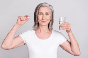 Photo of aged a senior woman that is happy with a positive smile and holding glass water and a pill for her Bio-identical hormone replacement therapy.